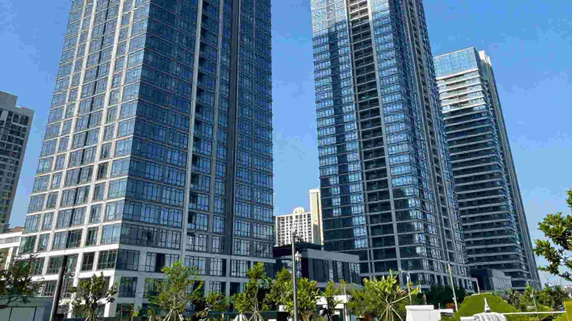 Tall modern residential skyscrapers at Godrej DMIC Greater Noida with glass windows standing under a clear blue sky with green plants at the base.